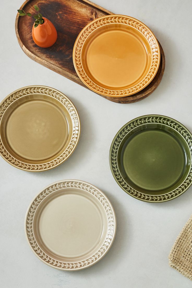 three plates with different colored rims on a wooden platter next to an orange