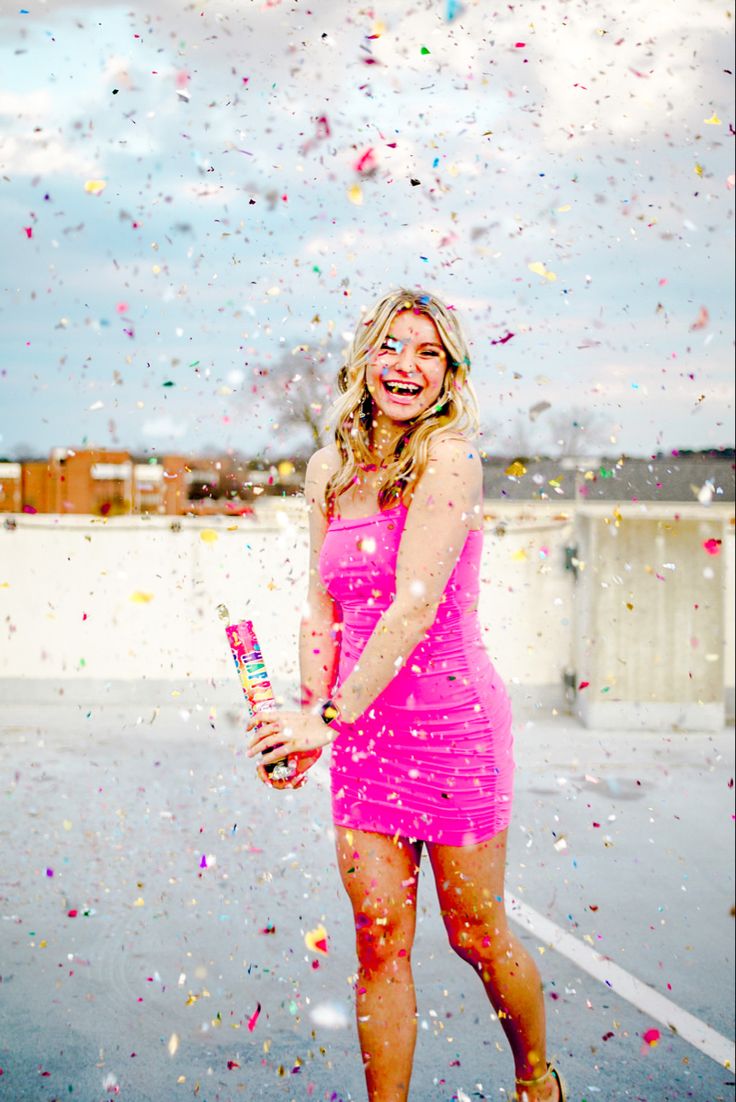 a woman in a pink dress is throwing confetti on her head and smiling