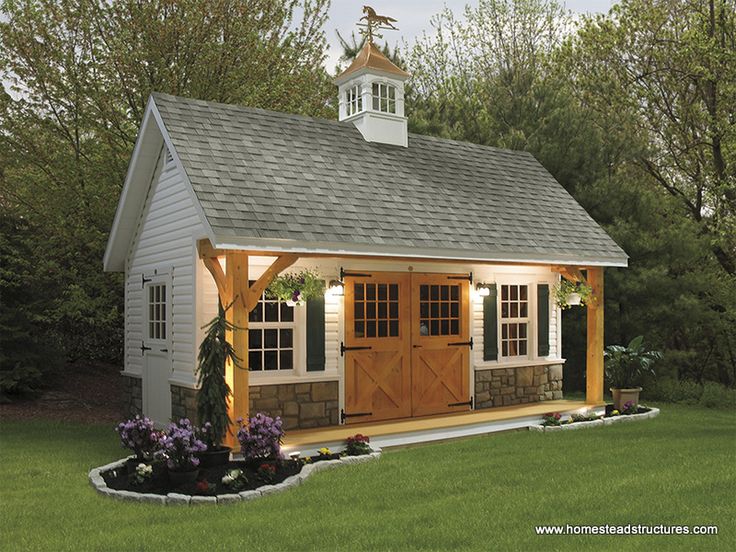 a small white shed with a wooden door and windows on the roof, surrounded by green grass