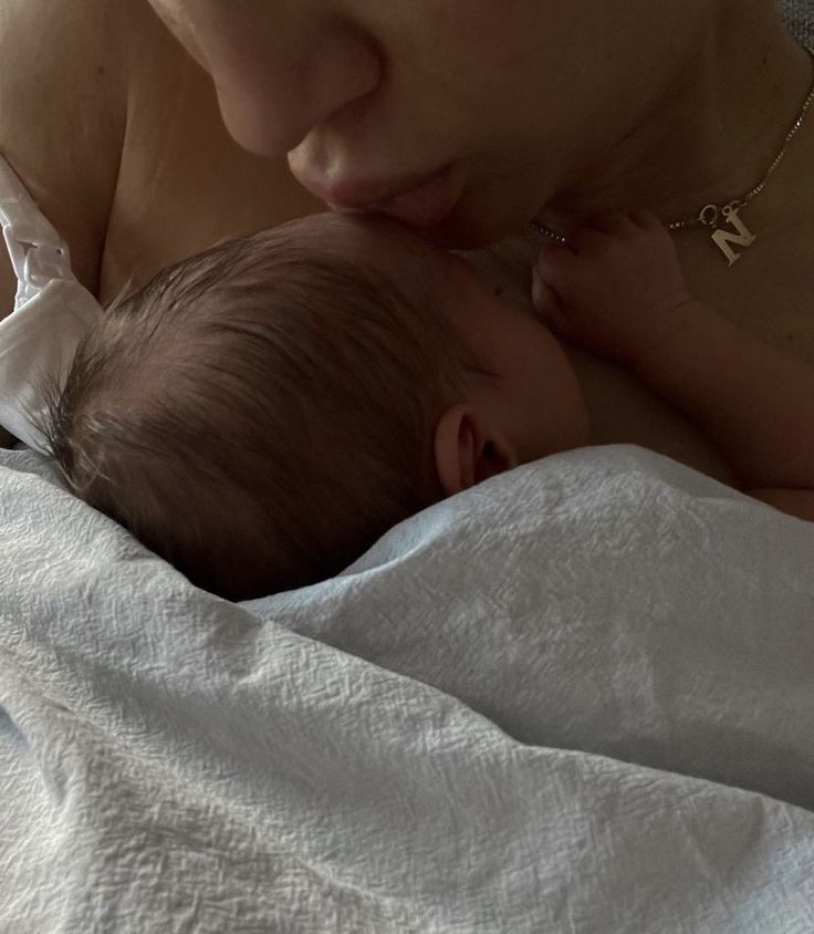 a woman holding a baby in her arms while laying on top of a bed with white sheets