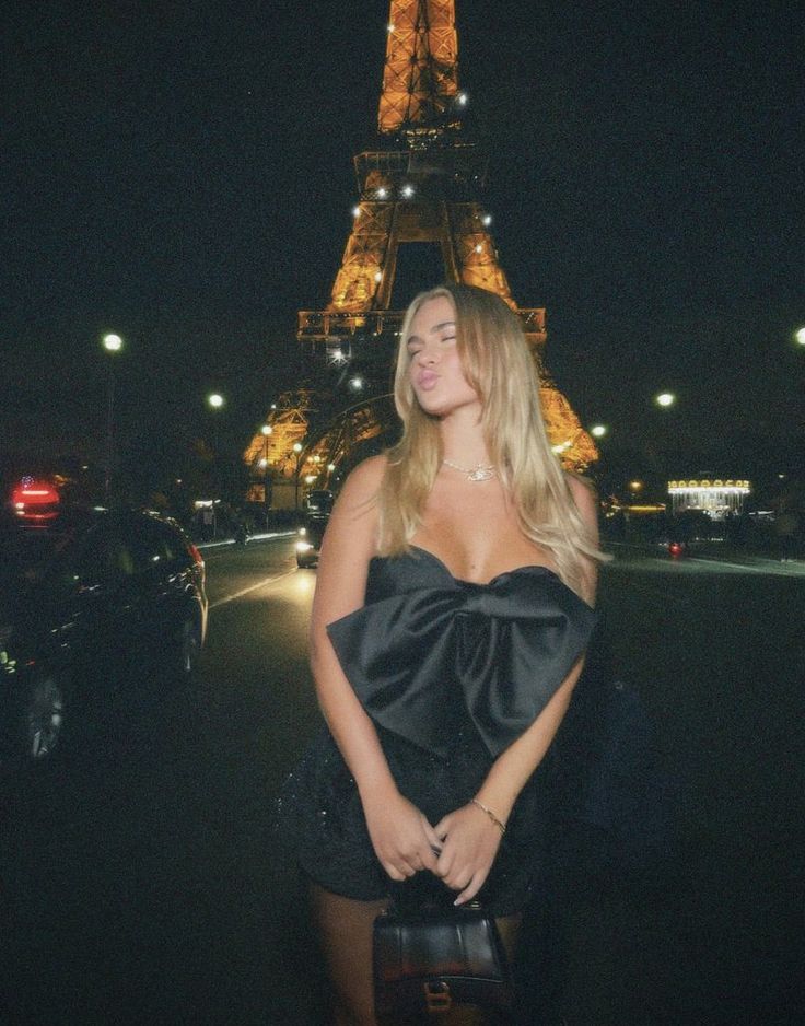 a woman standing in front of the eiffel tower at night with her hands on her hips