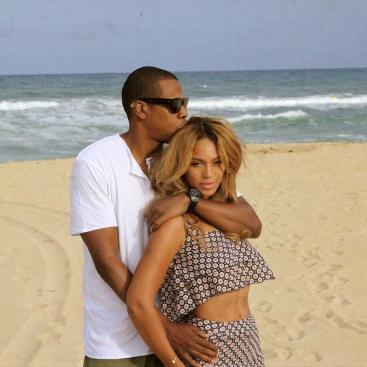 a man standing next to a woman on top of a sandy beach near the ocean