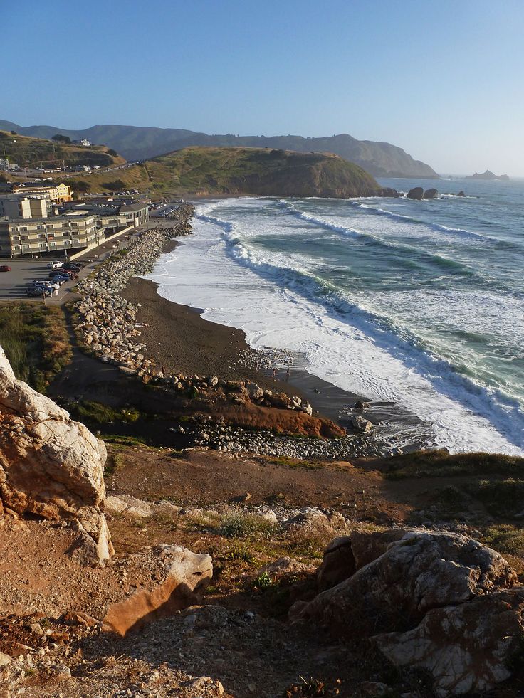 an ocean view from the top of a hill with houses on it and mountains in the background