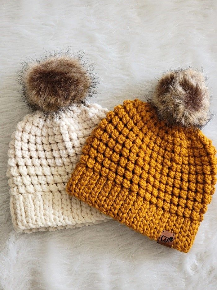 two crocheted beanies with pom - poms laying on top of each other