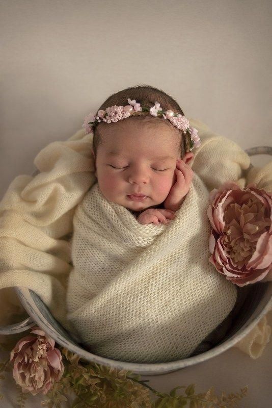 a newborn baby wrapped in a blanket and wearing a flower headband