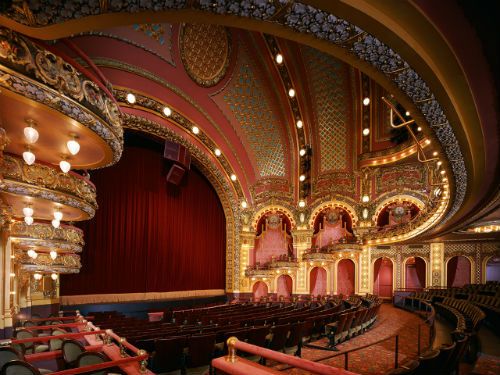 an empty theater with red seats and chandeliers