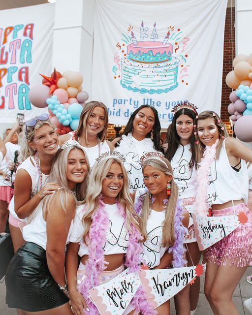 a group of young women standing next to each other in front of a birthday cake