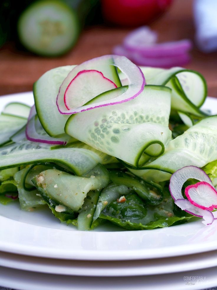 a white plate topped with cucumbers and green lettuce next to sliced radishes