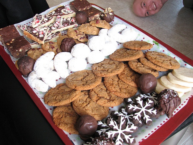 a tray filled with lots of different types of cookies and desserts next to a smiling child