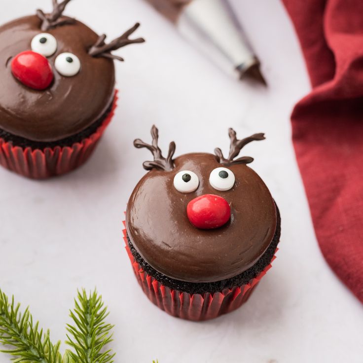 two cupcakes with chocolate frosting decorated as reindeer faces