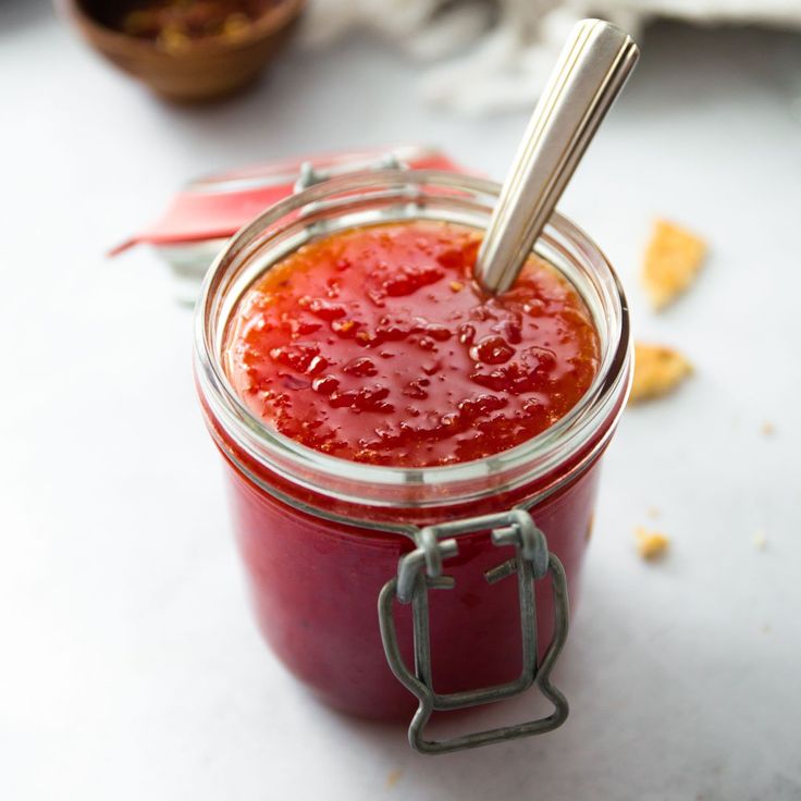 a jar filled with ketchup sitting on top of a table next to a spoon