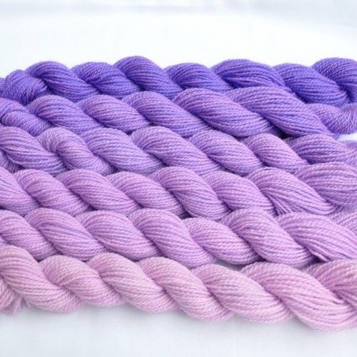 two skeins of purple and pink yarn on white tablecloth, close up