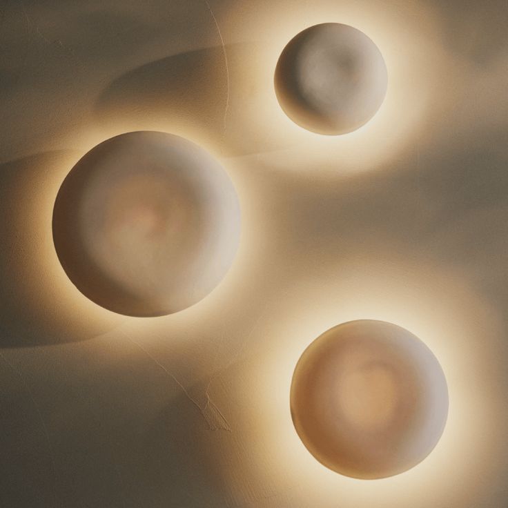 three white balls sitting next to each other on top of a table with light coming from them