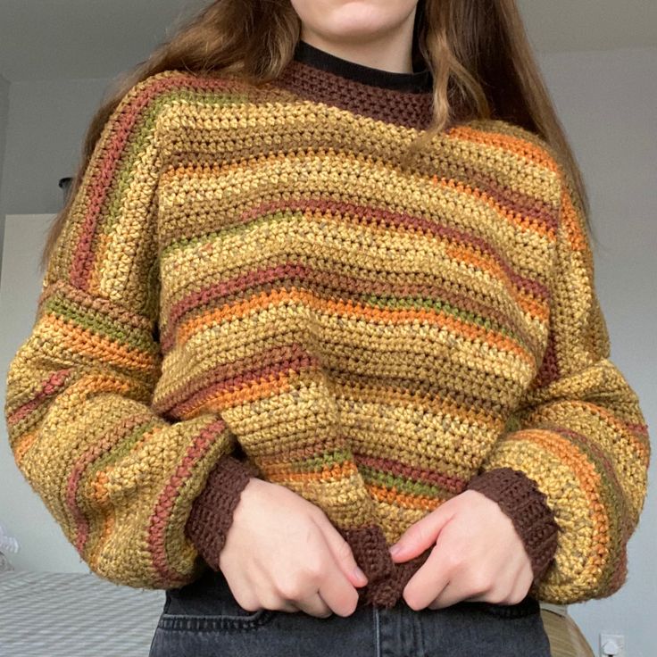 a woman standing in front of a bed with her hands on her hips, wearing a multicolored sweater