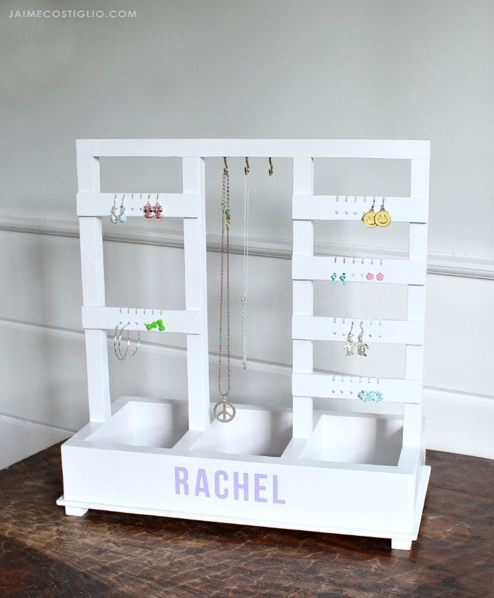 a white jewelry rack with earrings and necklaces on the top shelf that says rachel