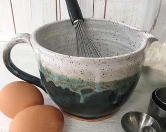 two eggs and an egg whisk in a ceramic bowl on a white table