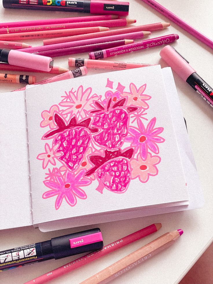 an open notebook with pink flowers on it surrounded by colored pencils