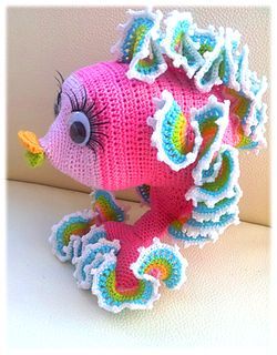 a crocheted stuffed animal with pink hair and blue eyes sitting on top of a white surface