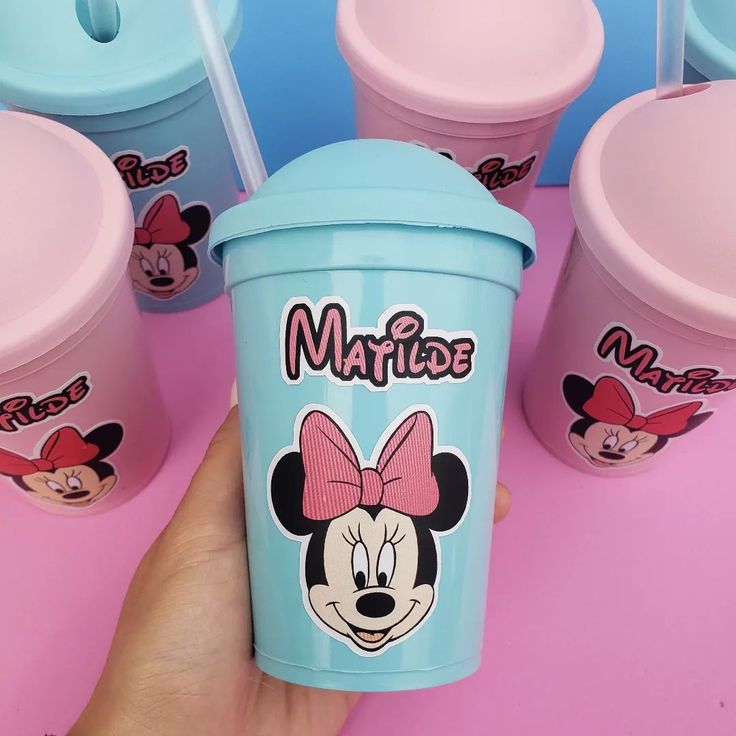 a person holding up a cup with mickey mouse on it and other cups in the background