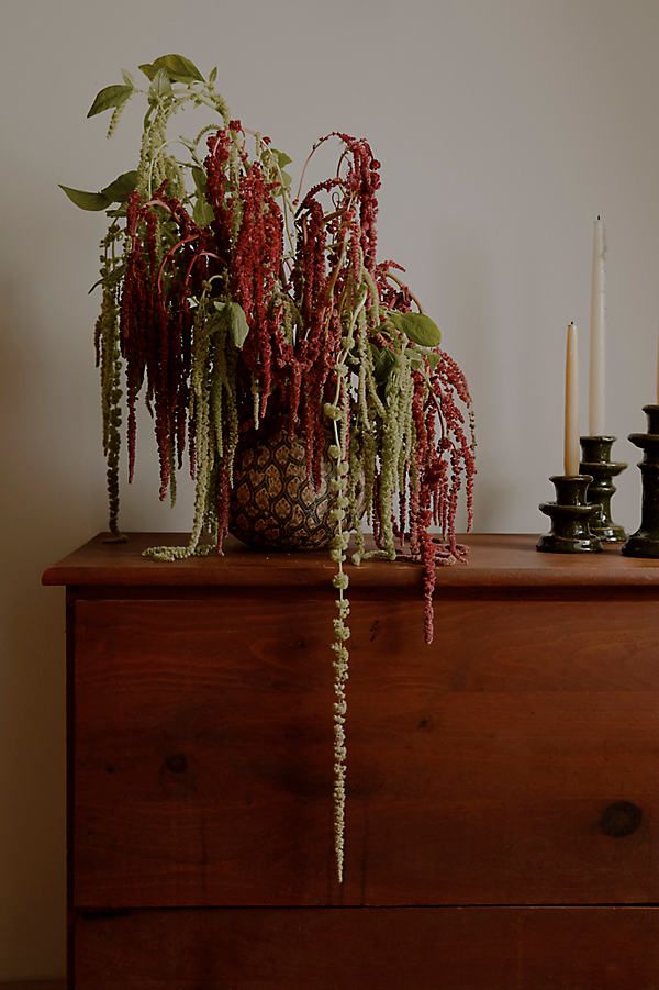 a wooden dresser topped with a potted plant next to two candles and a candle holder