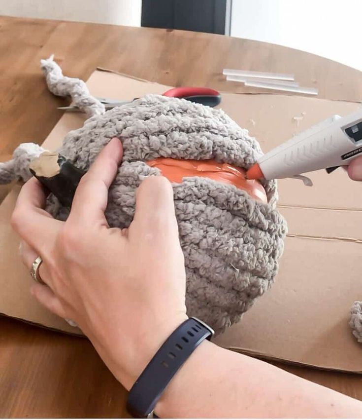 a person is crocheting the yarn on top of a piece of cardboard with scissors