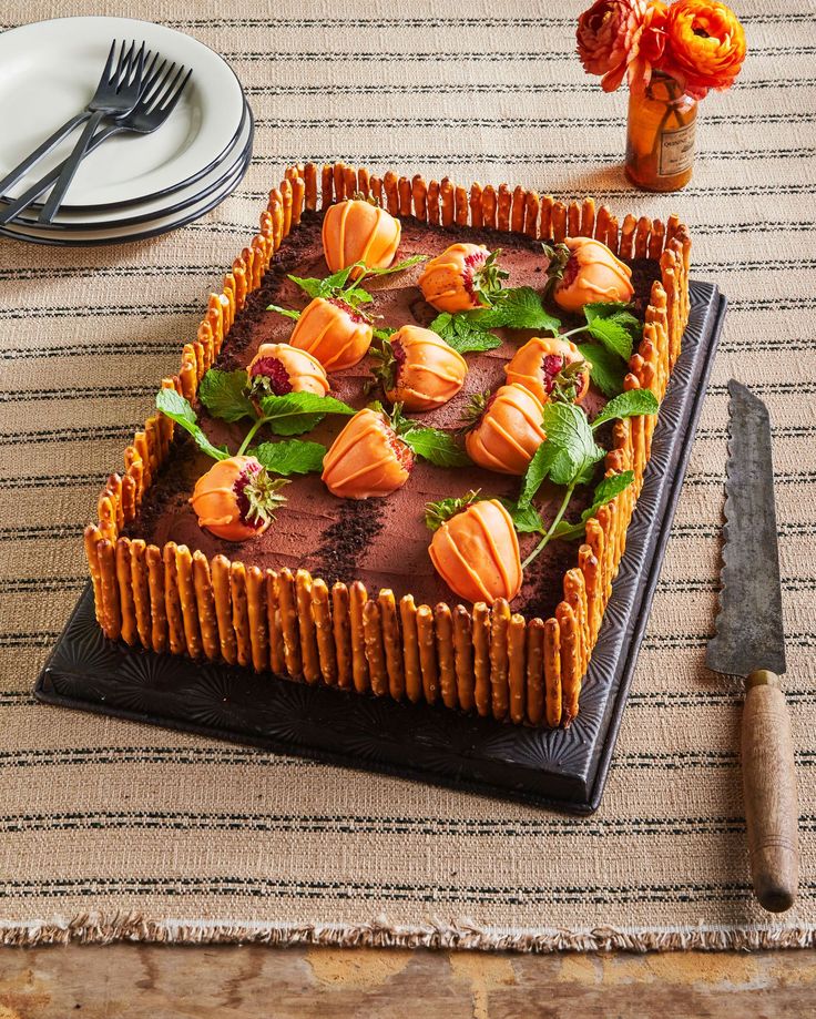 a chocolate cake decorated with orange flowers and leaves on a table next to silverware