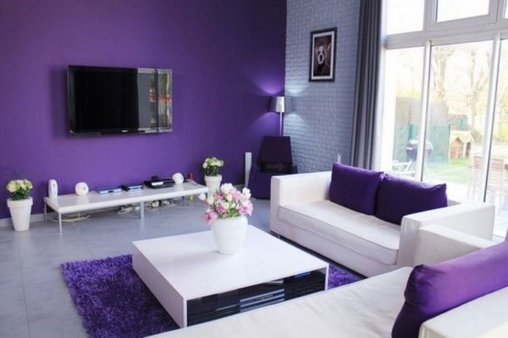 a living room with purple walls and white furniture in the center, along with a large flat screen tv mounted on the wall