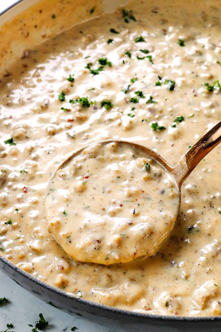 a ladle full of cream sauce being stirred by a wooden spoon in a skillet