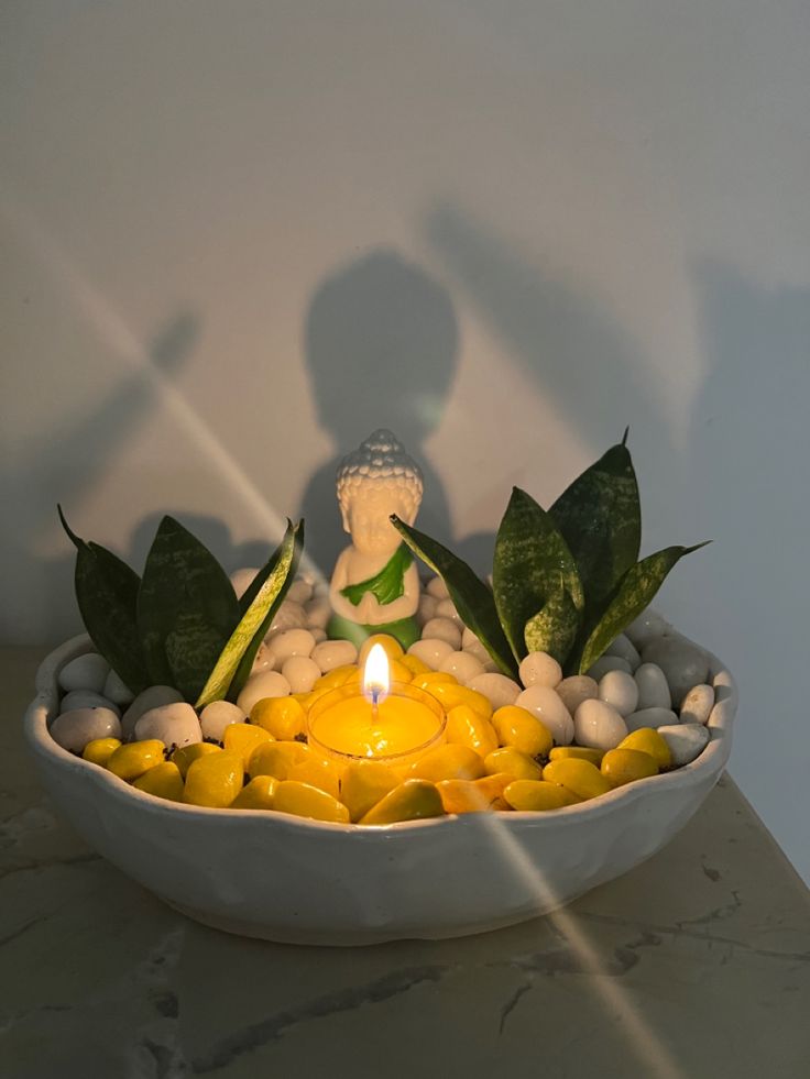 a bowl filled with rocks and candles on top of a table next to a buddha figurine