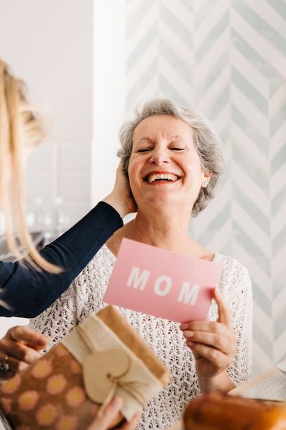 two women holding gifts and smiling at each other while another woman holds up a card with the word mom on it