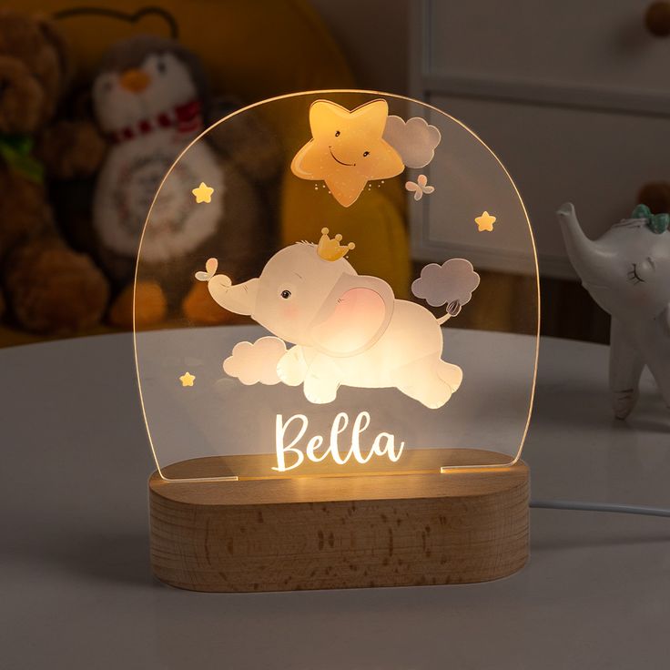 an illuminated baby elephant in a glass dome on a wooden base with the name bella underneath it