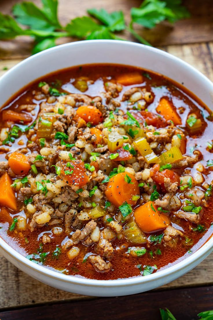 a white bowl filled with meat and vegetable soup on top of a wooden cutting board