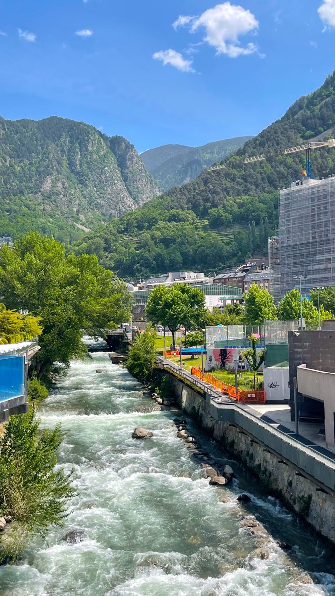 a river running through a lush green hillside next to a tall building with mountains in the background