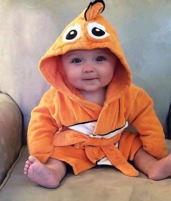 a baby in a orange robe sitting on a couch wearing a paco face hoodie