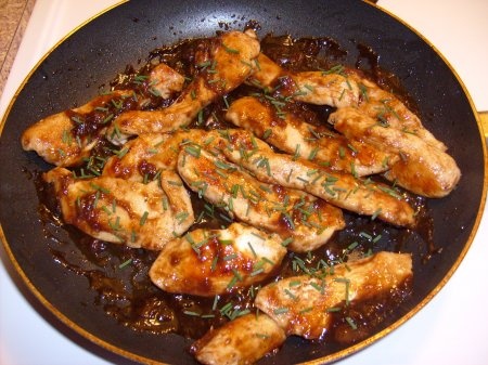 some chicken is cooking in a frying pan on the stove with sauce and garnishes