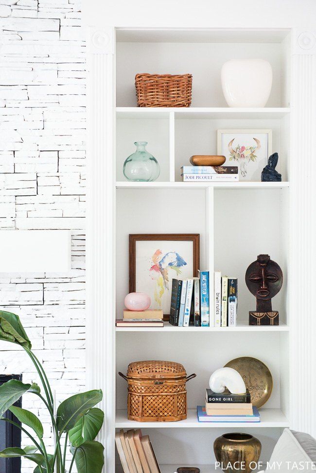 a white book shelf filled with books next to a potted plant and other items