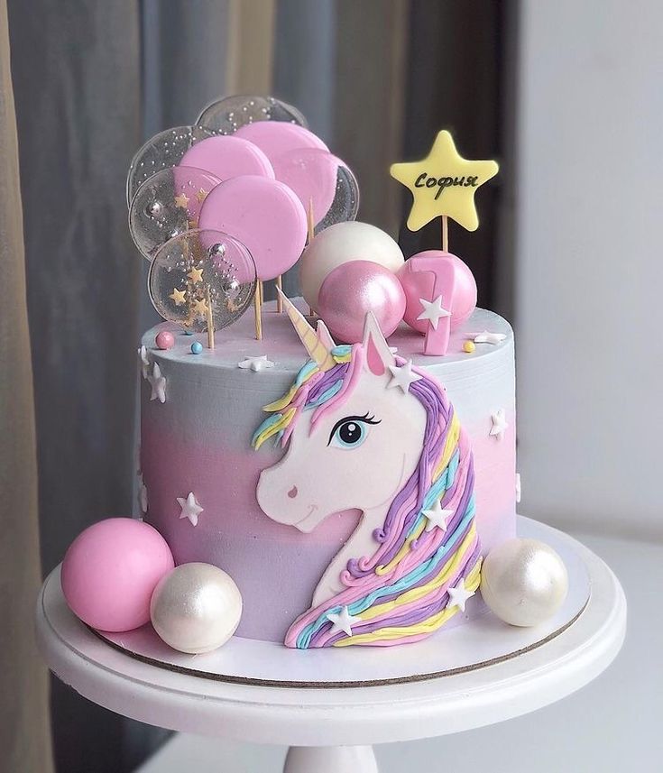 a cake decorated with pink, white and blue icing has a unicorn on it