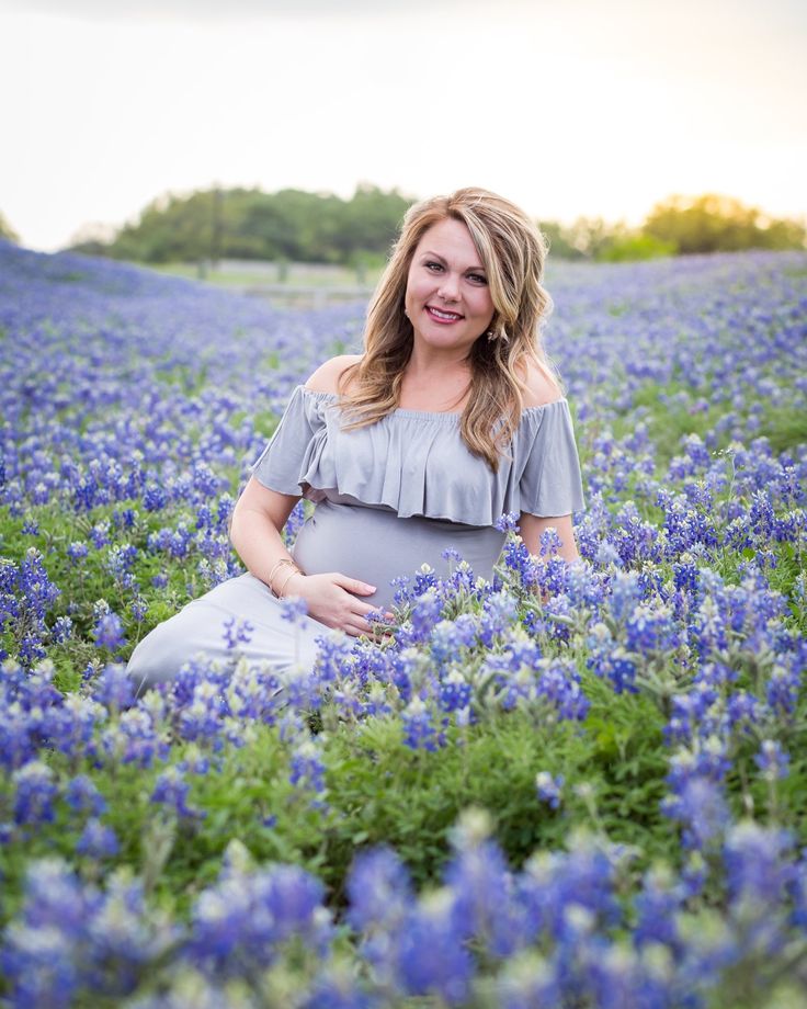 a pregnant woman sitting in a field of blue flowers