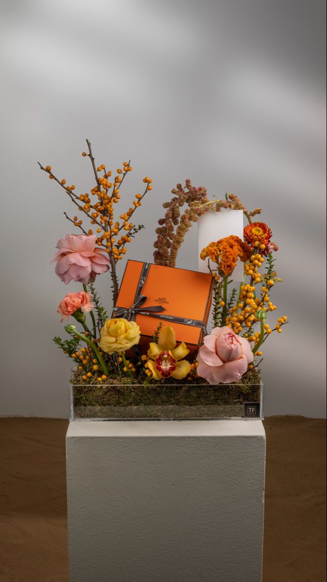 an arrangement of flowers in a vase on top of a white box with orange and yellow accents