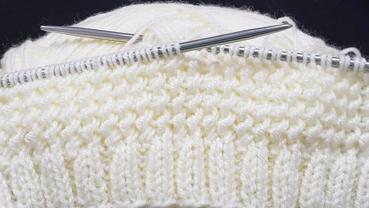 two knitting needles on top of a white knitted hat