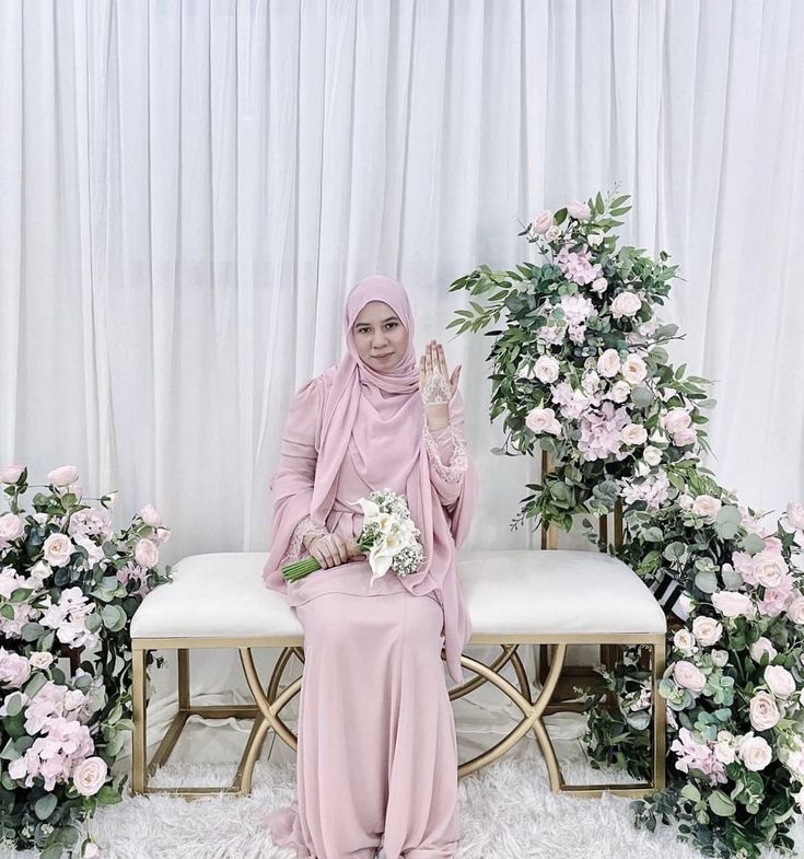 a woman in a pink hijab sitting on a bench with flowers around her