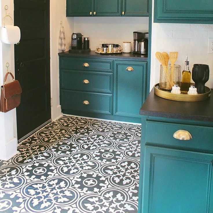 a kitchen with teal cabinets and black counter tops, white tile flooring and gold accents