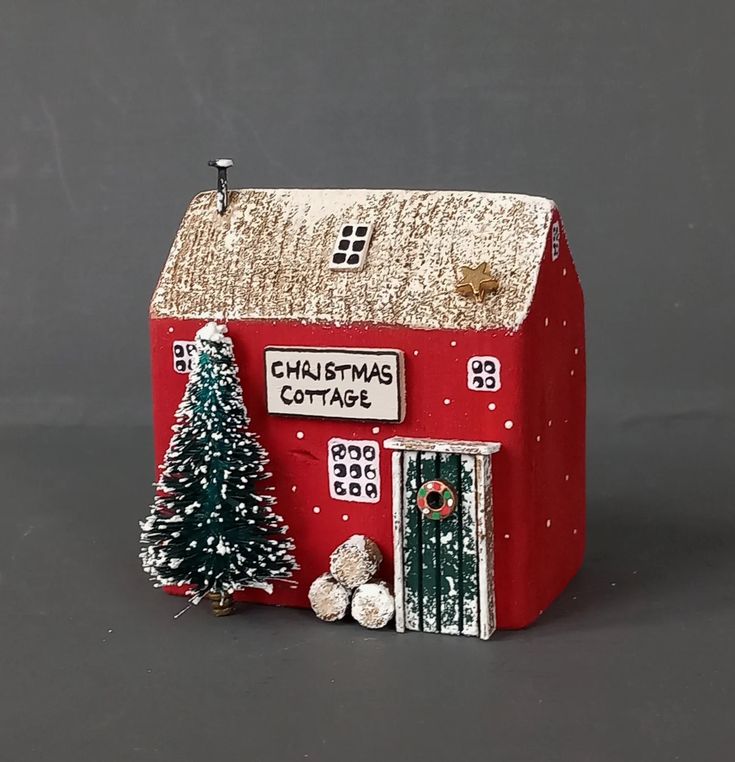 a small red house with a christmas tree on the front and sign that says christmas cottage