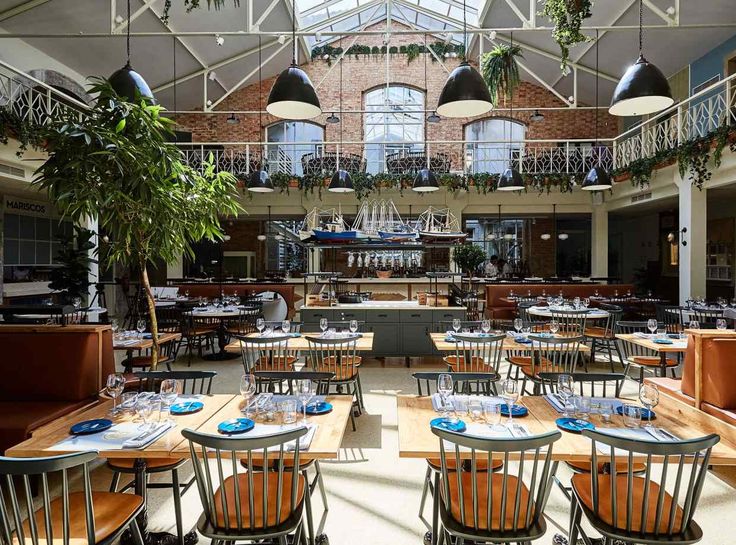 an indoor dining area with tables, chairs and potted plants in the middle of it