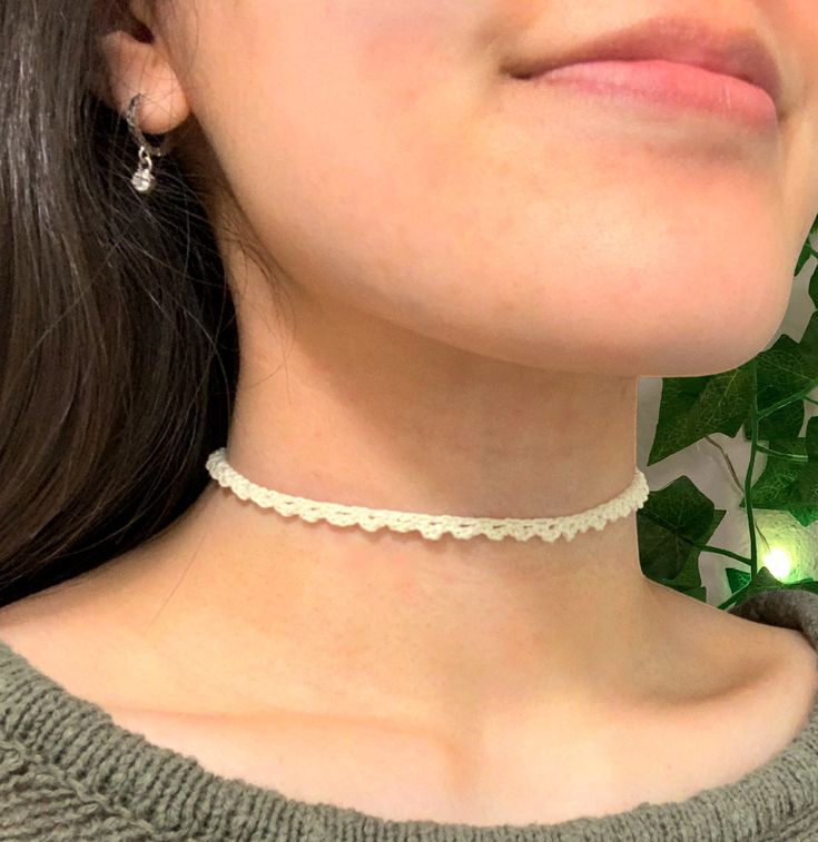 a close up of a woman wearing a necklace with flowers behind her head and green leaves in the background