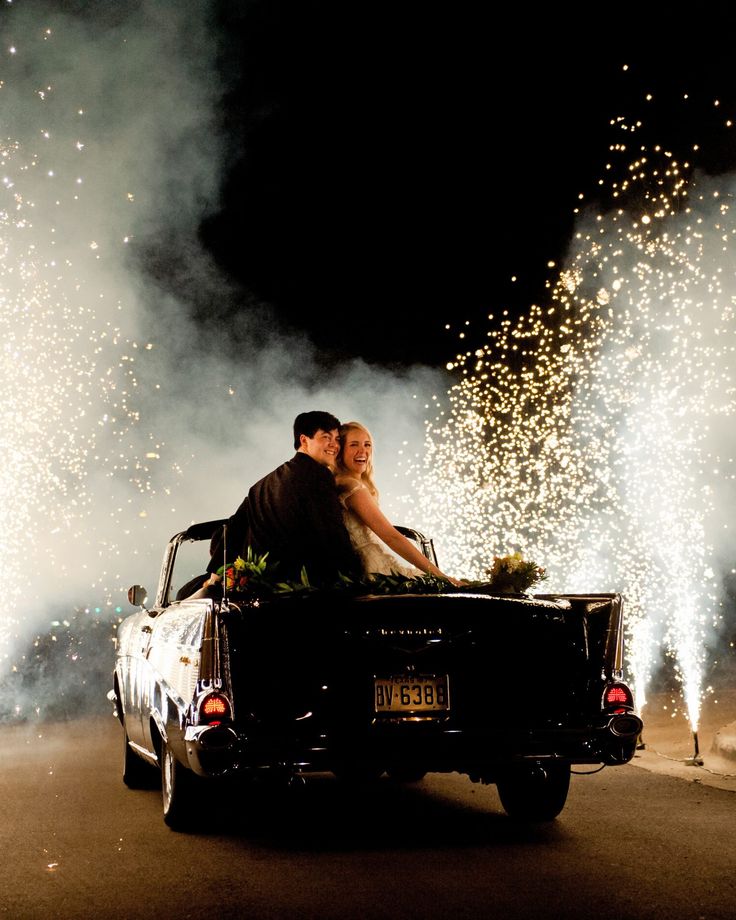 a bride and groom sitting in the back of a truck with fireworks coming out of it