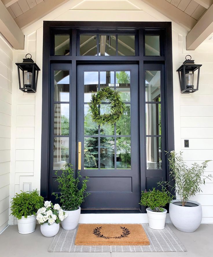 the front door is decorated with potted plants and two wreaths on each side