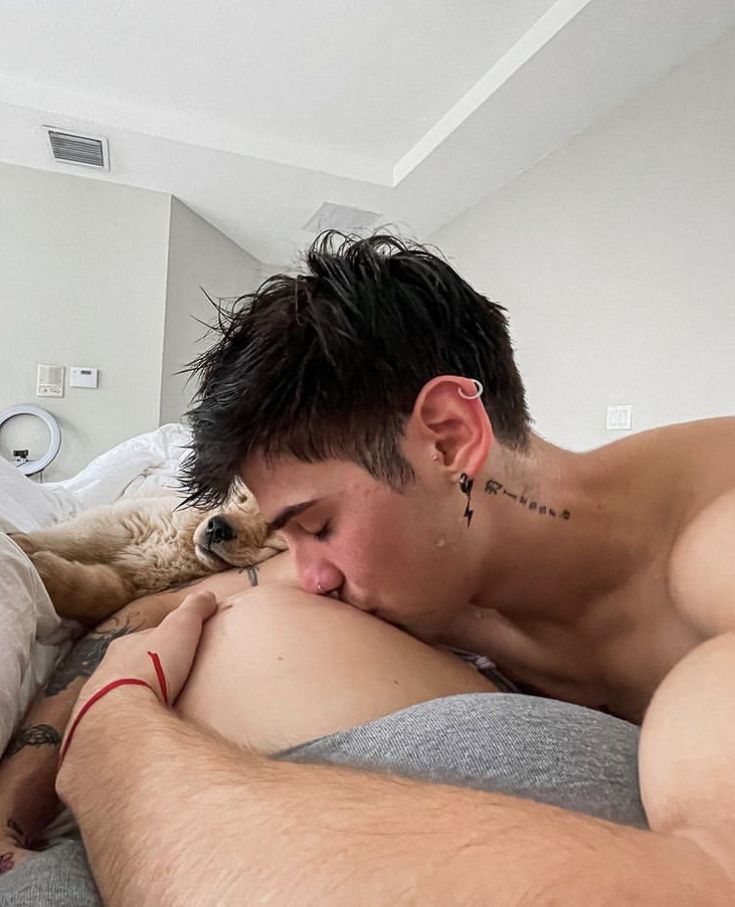 a shirtless man laying in bed with his arm around a dog's head