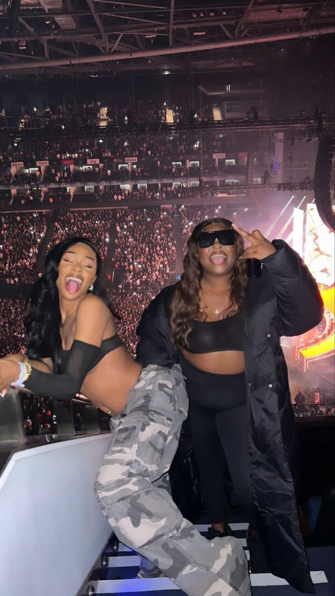 two women standing on top of a stage in front of an audience at a concert