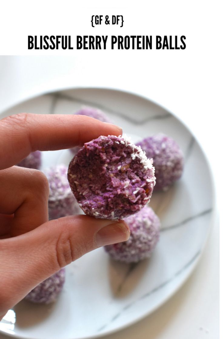 a hand holding a berry protein ball on a plate